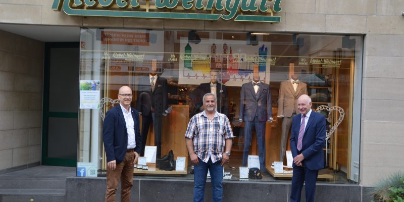 Oberbürgermeister Dirk Meid, Künstler Mohammad Taherinia und Firmeninhaber Hans-Paul Hiebel von Herrenausstattung Hiebel-Weingart stehen vor dem Schaufenster des Geschäfts.